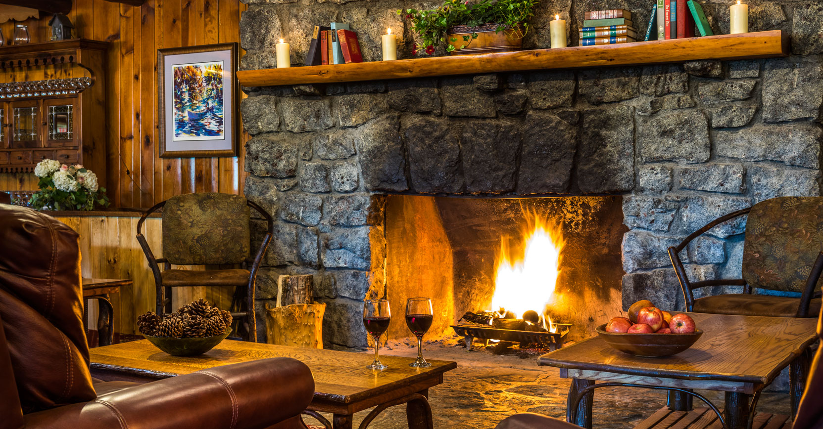 A roaring fireplace with two glasses of red wine in front of it