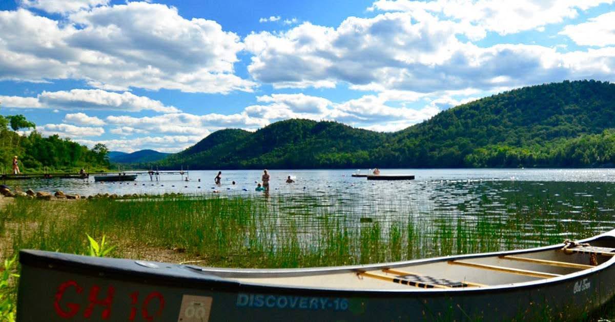 a canoe on the shores of thirteenth lake with people swimming in the background