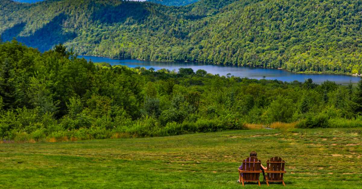 two adirondack chairs in a grassy field overlooking thirteenth lake